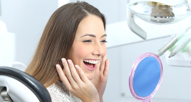 Frau auf dem Behandlungsstuhl beim Zahnarzt strahlt in einen Handspiegel