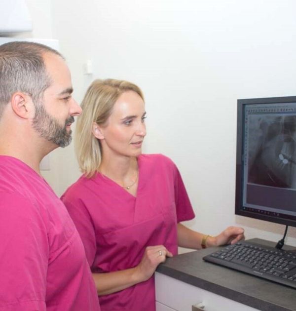 Zahnarzt Sebastian Koller schaut sich mit einer zahnmedizinischen Fachangestellten von DentisBavaria die Röntgenaufnahmen eines Gebisses auf dem Bildschirm eines Standrechners an