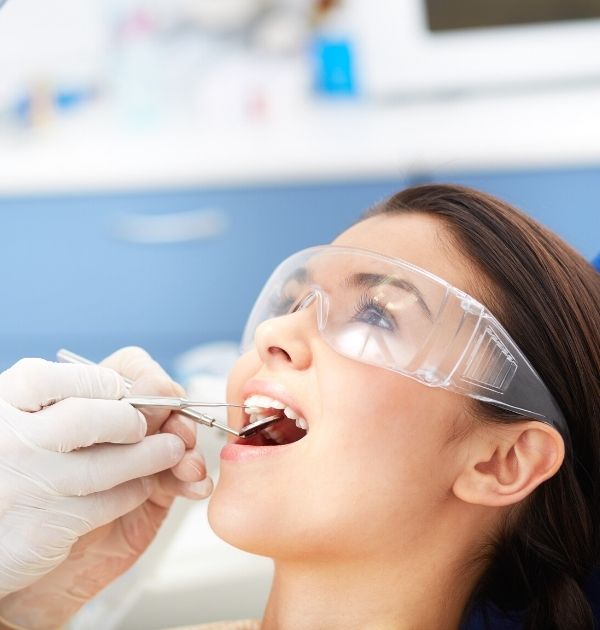 Patientin mit Schutzbrille bei einer zahnmedizinischen Untersuchung mit Dentalspiegel und Scaler