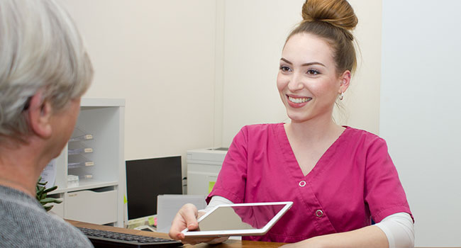 Lächelnde zahnmedizinische Fachangestellte zeigt einem Patienten etwas auf dem Tablet