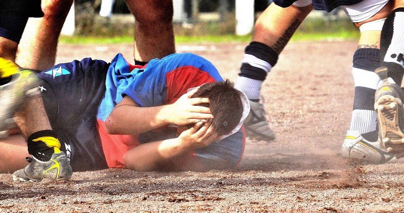 Mann liegt auf dem Boden und schützt seinen Kopf beim Rugby-Spiel