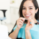 Patientin setzt sich auf dem Behandlungsstuhl in der Praxis eine unsichtbare Zahnschiene ein
