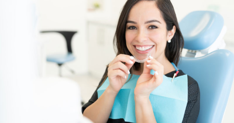 Patientin setzt sich auf dem Behandlungsstuhl in der Praxis eine unsichtbare Zahnschiene ein
